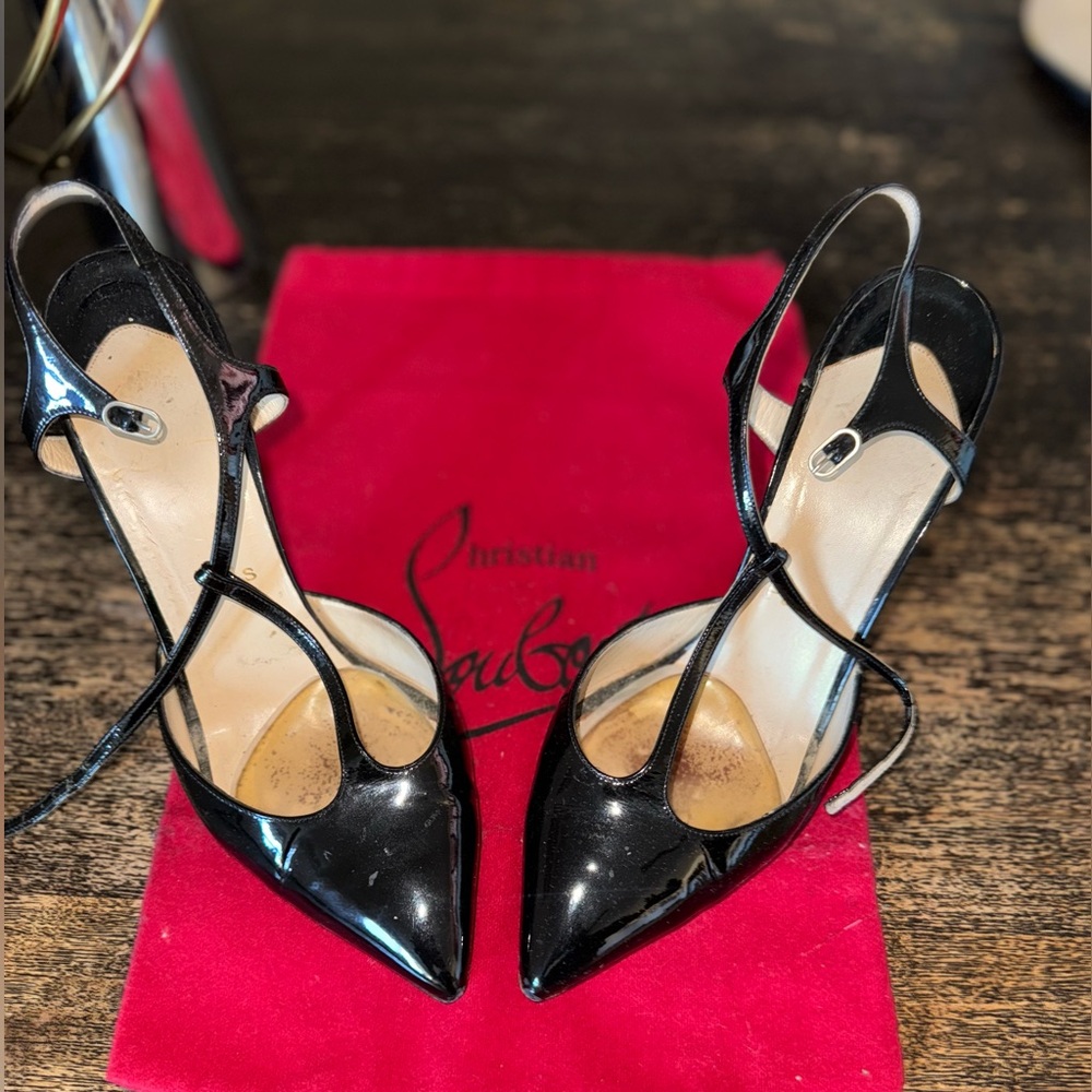 Patent leather pump with ankle strap. Left strap is shorter than right one.